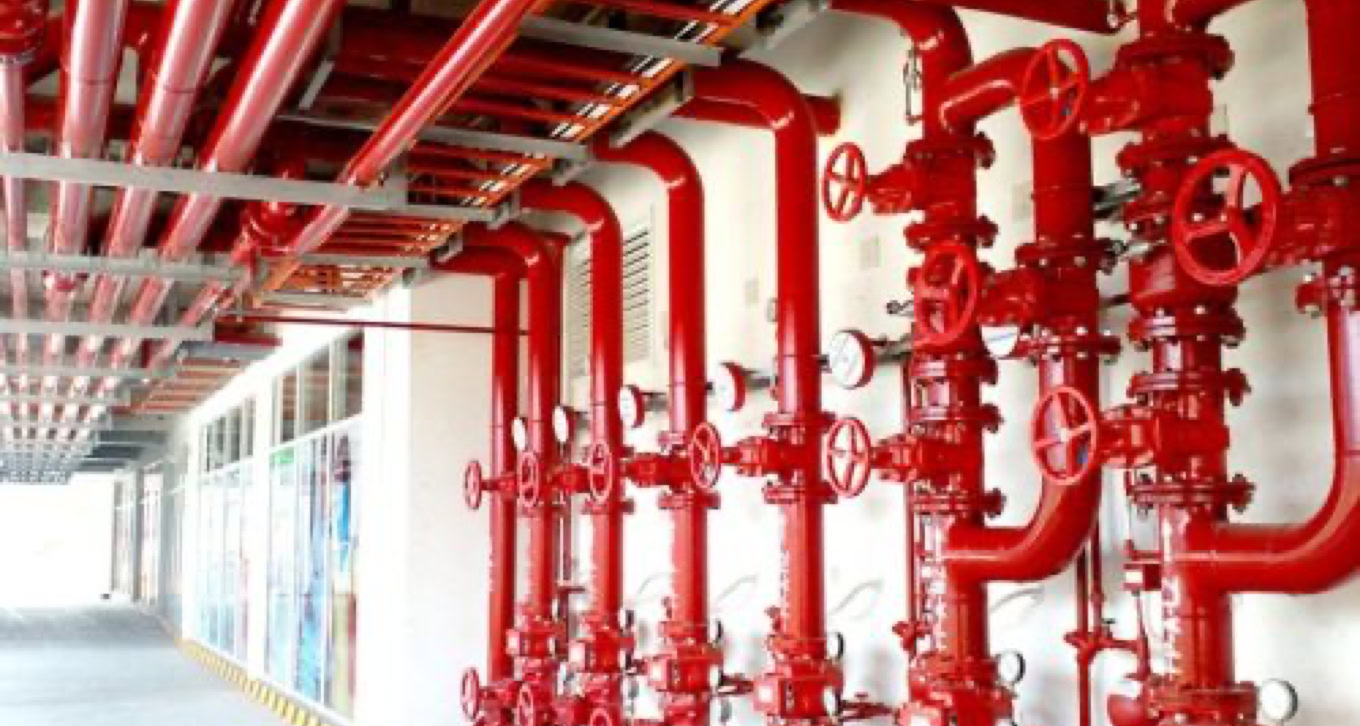 Red industrial pipes and valves mounted on a wall.