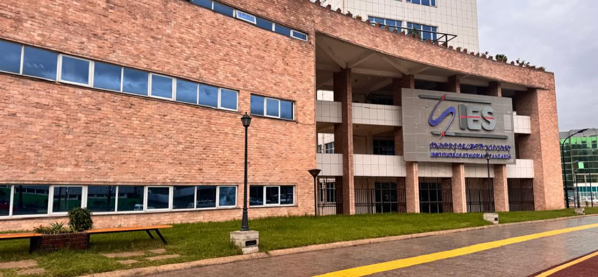 Tall modern apartment building with multiple balconies and a gated entrance.