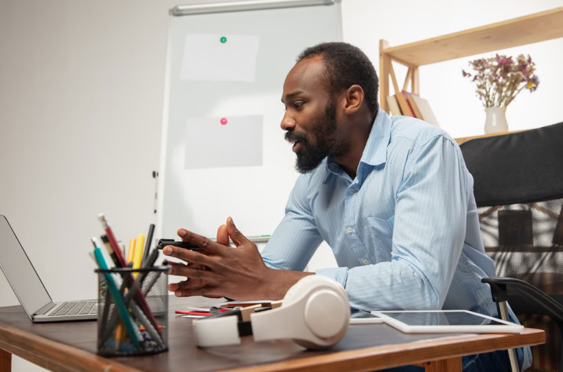 Man sitting at a desk with a laptop, wearing a blue shirt, and looking focused.