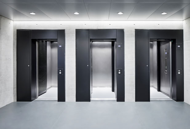Three modern elevator doors in a well-lit hallway.