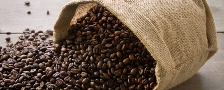A burlap sack spilling roasted coffee beans onto a wooden surface.