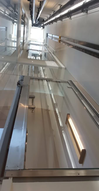 Looking up inside a modern glass elevator shaft with visible lights and metal rails.