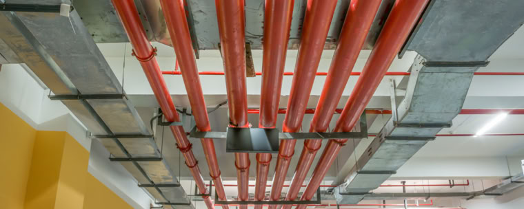 Red pipes and metal ducts on a ceiling in an industrial or commercial building.
