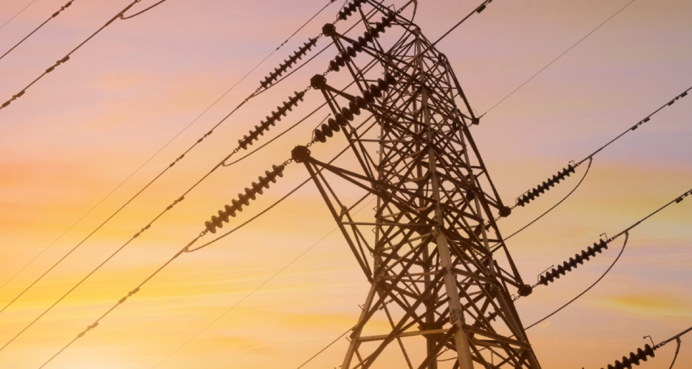 High-voltage power lines and tower against a sunset sky.