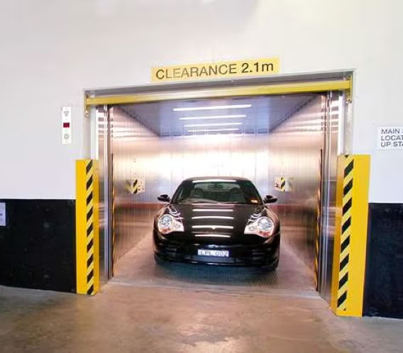 A car entering a parking garage elevator with a clearance sign above.